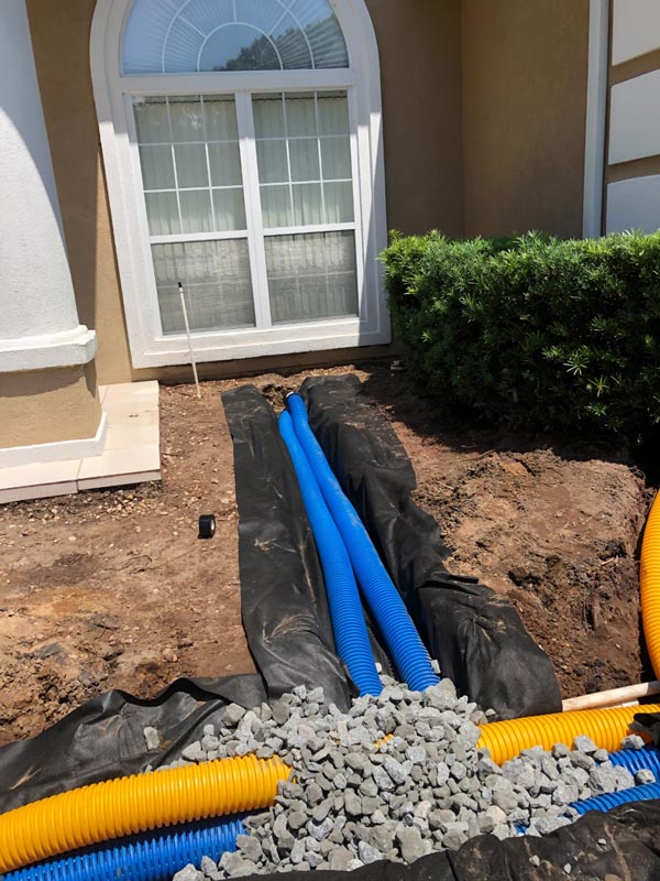 Blue and yellow drain pipes tied together in a gravel trench