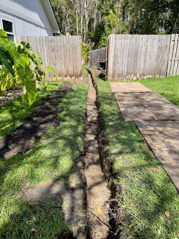 Narrow excavated trench running along a fenced backyard