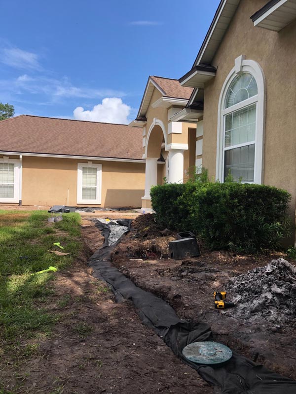 Fabric-lined French drain trench with gravel beside a home